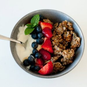 bowl of hemp granola with blueberries and strawberries with yoghurt and spoon on a white background